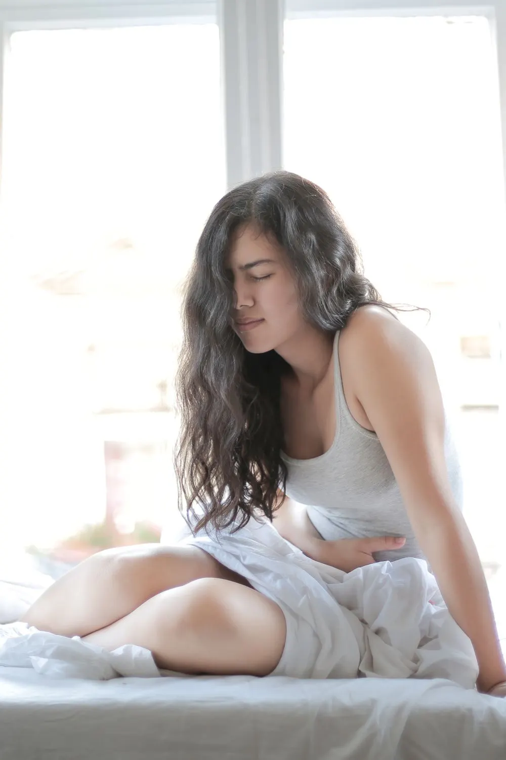 Woman sitting on a bed holding her stomach