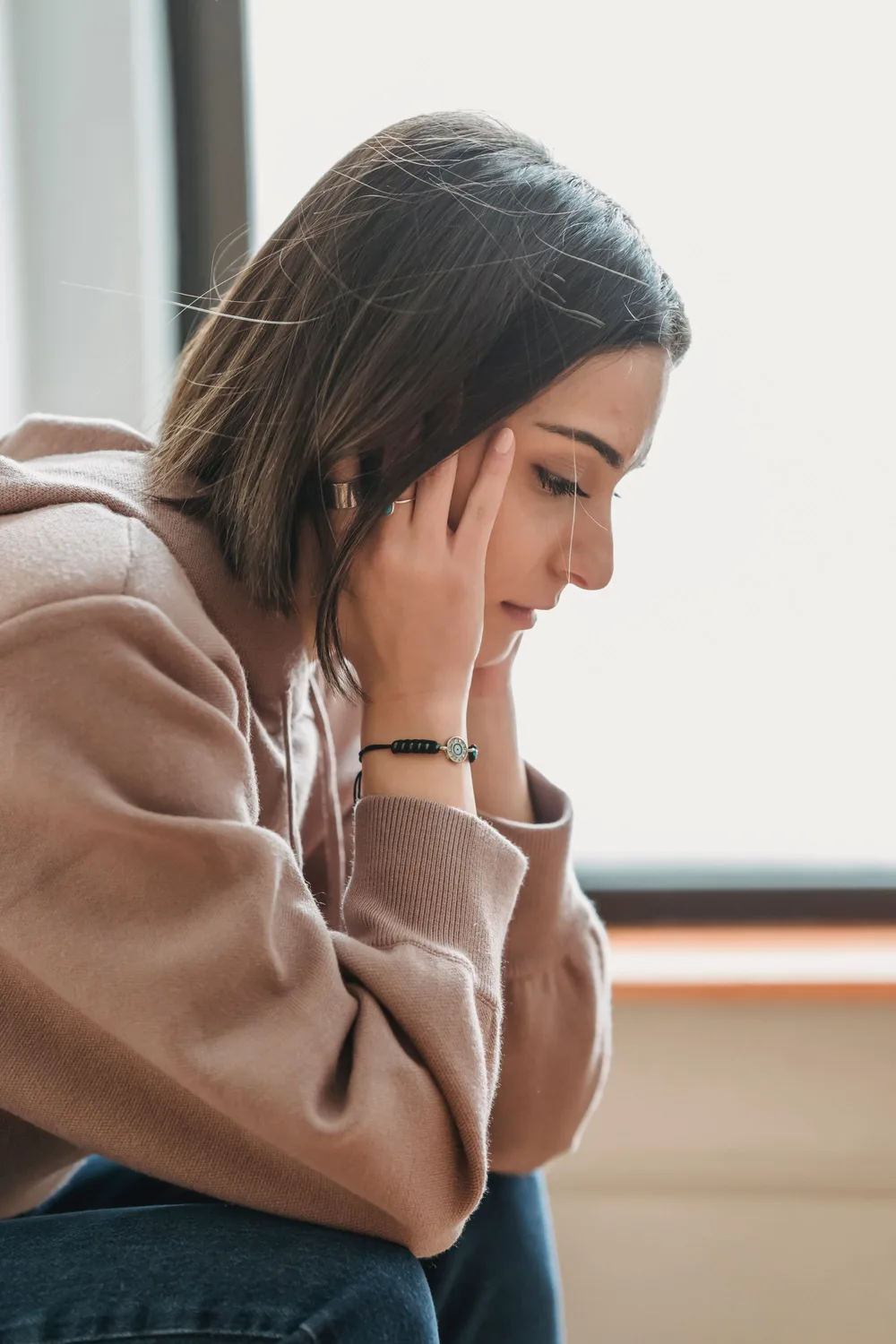 Woman sitting by a window with her head resting in her hands